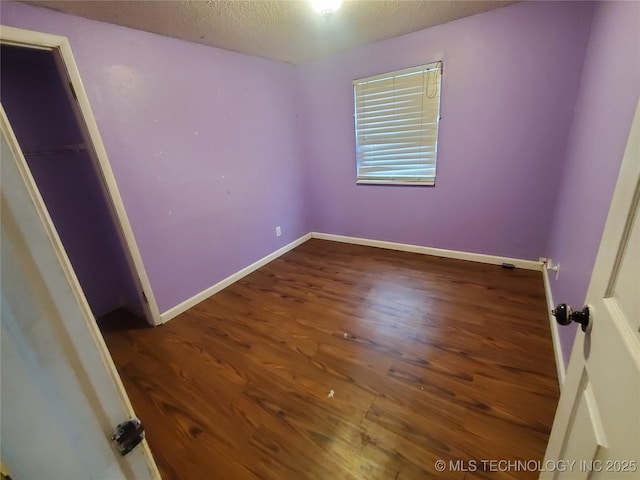 unfurnished bedroom with a walk in closet, a textured ceiling, dark hardwood / wood-style flooring, and a closet