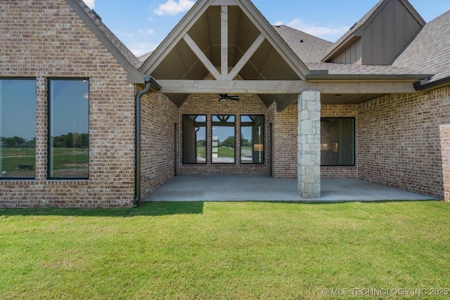entrance to property featuring board and batten siding, a ceiling fan, a lawn, a patio area, and brick siding