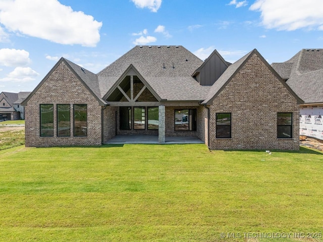 rear view of property with a lawn, a patio, roof with shingles, and brick siding
