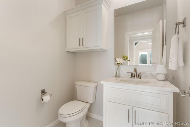 half bath with toilet, baseboards, and vanity
