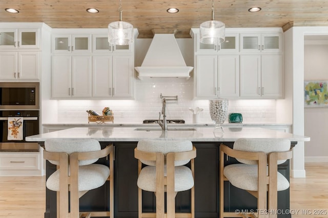 kitchen featuring white cabinets, appliances with stainless steel finishes, light wood-style floors, premium range hood, and wooden ceiling