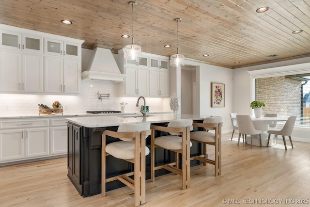 kitchen with wooden ceiling, white cabinetry, custom exhaust hood, and a sink