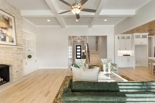 living area with ceiling fan, a fireplace, beamed ceiling, light wood finished floors, and ornamental molding