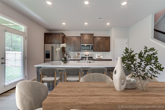 kitchen with dark brown cabinets, stainless steel appliances, a breakfast bar area, and tasteful backsplash