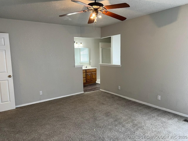 unfurnished bedroom featuring a textured ceiling, ensuite bathroom, dark carpet, and ceiling fan