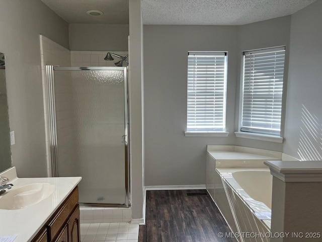 bathroom with plus walk in shower, a textured ceiling, vanity, and a healthy amount of sunlight