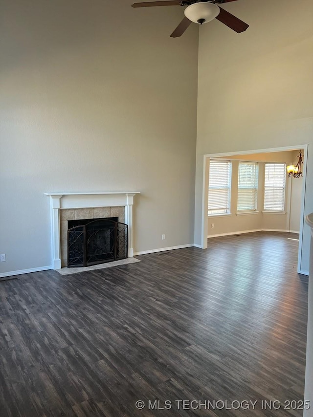 unfurnished living room with ceiling fan, dark wood-type flooring, and a tiled fireplace