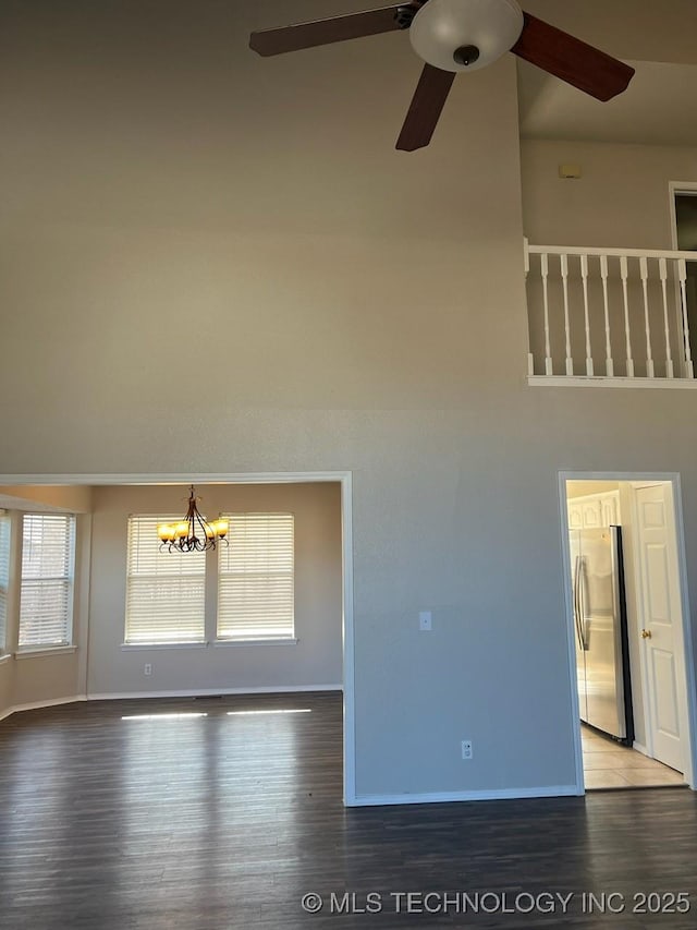 unfurnished living room featuring ceiling fan with notable chandelier and dark wood-type flooring