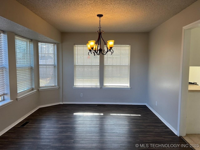 unfurnished dining area featuring dark hardwood / wood-style flooring, a textured ceiling, and an inviting chandelier