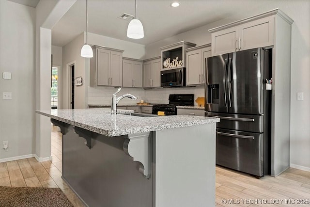 kitchen with a center island with sink, sink, stainless steel appliances, and hanging light fixtures