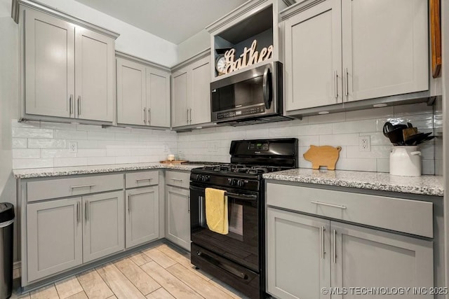 kitchen featuring black range with gas stovetop, light stone countertops, light wood-type flooring, and tasteful backsplash