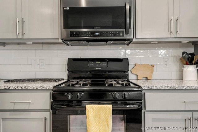 kitchen featuring black gas range oven, tasteful backsplash, and light stone counters