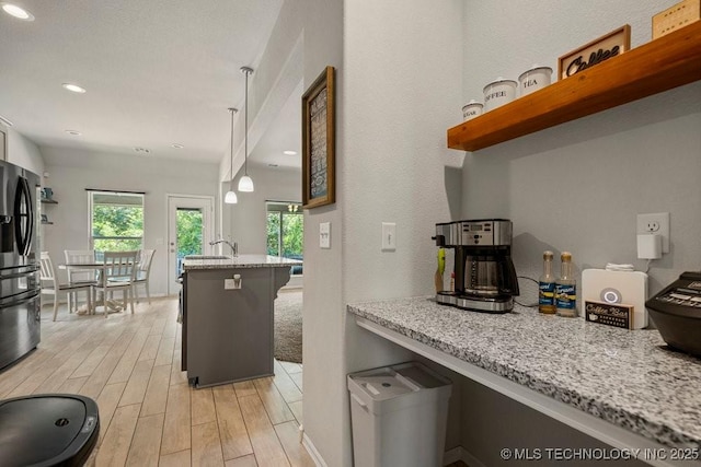 kitchen featuring pendant lighting, stainless steel fridge, light stone countertops, and kitchen peninsula