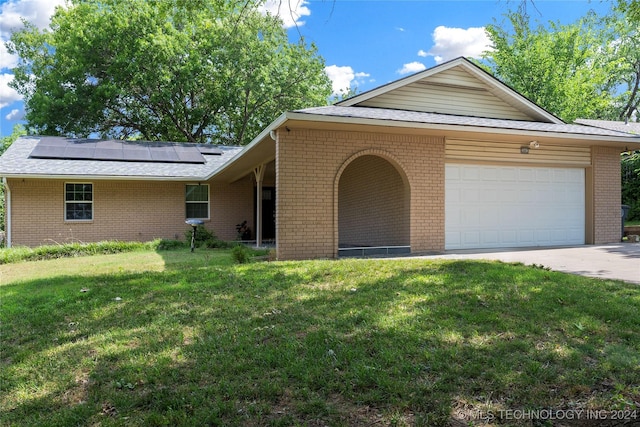 ranch-style home with a garage, a front yard, and solar panels