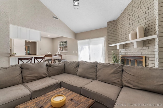 living room featuring a brick fireplace, a textured ceiling, and vaulted ceiling