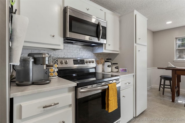 kitchen featuring appliances with stainless steel finishes, tasteful backsplash, a textured ceiling, white cabinets, and light tile patterned flooring