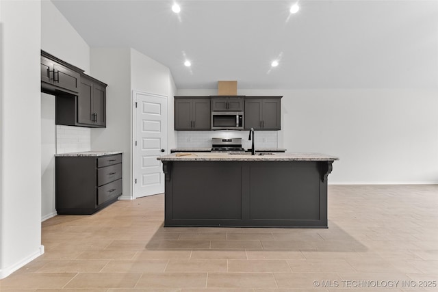 kitchen with light stone countertops, a kitchen island with sink, and appliances with stainless steel finishes