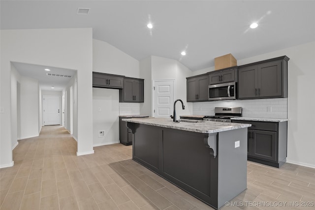 kitchen featuring light stone countertops, sink, stainless steel appliances, vaulted ceiling, and a center island with sink