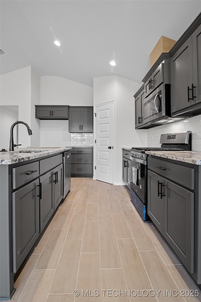 kitchen with appliances with stainless steel finishes, sink, lofted ceiling, and gray cabinetry