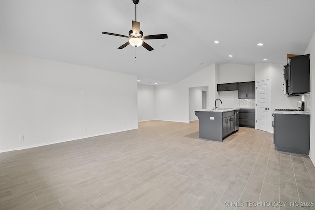 kitchen with a center island with sink, sink, vaulted ceiling, ceiling fan, and decorative backsplash