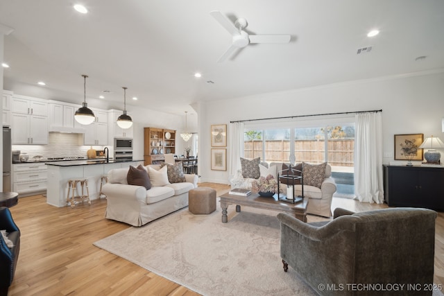 living area featuring a ceiling fan, visible vents, light wood-style flooring, recessed lighting, and ornamental molding