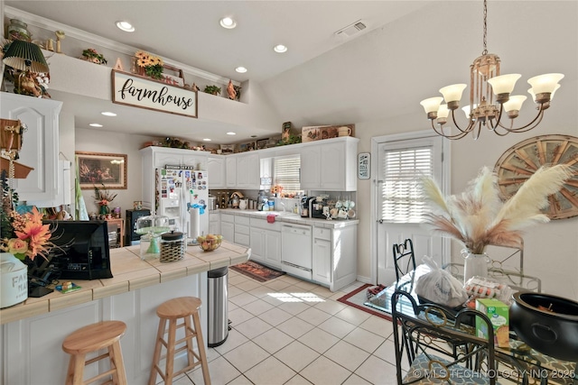 kitchen with white appliances, light tile patterned floors, tile countertops, an inviting chandelier, and white cabinets