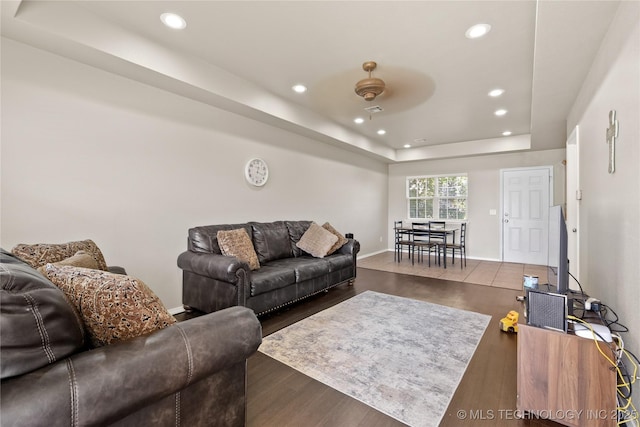 living room with dark hardwood / wood-style flooring, a raised ceiling, and ceiling fan