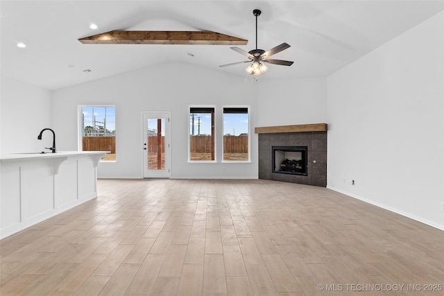 unfurnished living room featuring a tiled fireplace, vaulted ceiling with beams, and ceiling fan