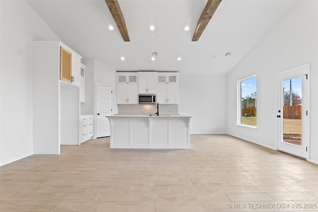 kitchen featuring tasteful backsplash, white cabinetry, an island with sink, sink, and vaulted ceiling with beams