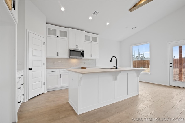 kitchen with lofted ceiling with beams, white cabinets, and a center island with sink