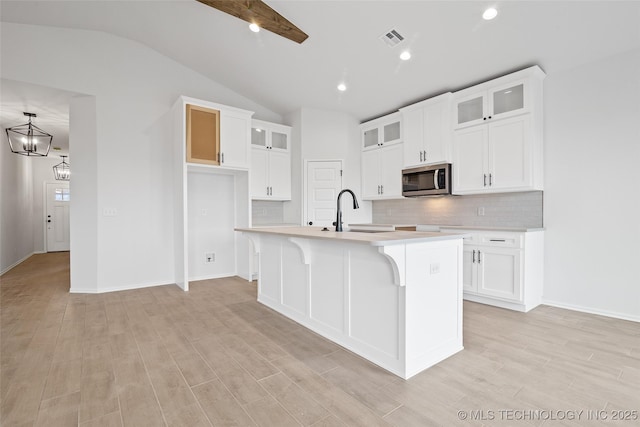 kitchen with sink, vaulted ceiling with beams, a center island with sink, light hardwood / wood-style floors, and white cabinets