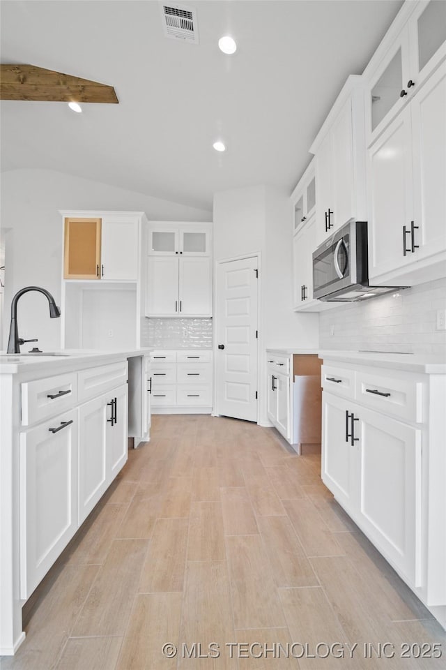 kitchen featuring backsplash, sink, vaulted ceiling, and white cabinets