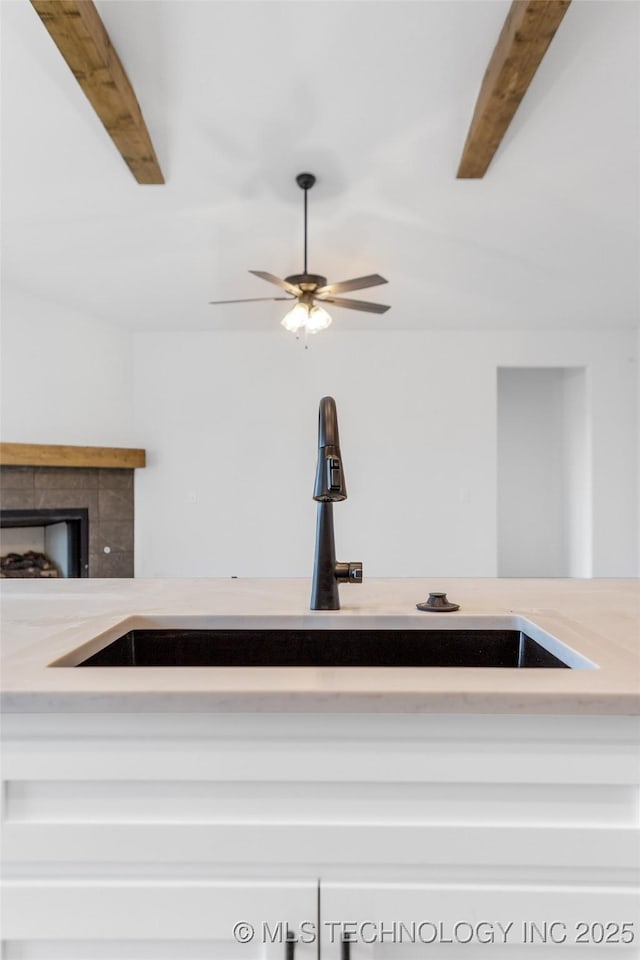 kitchen featuring a tiled fireplace, ceiling fan, sink, and beam ceiling