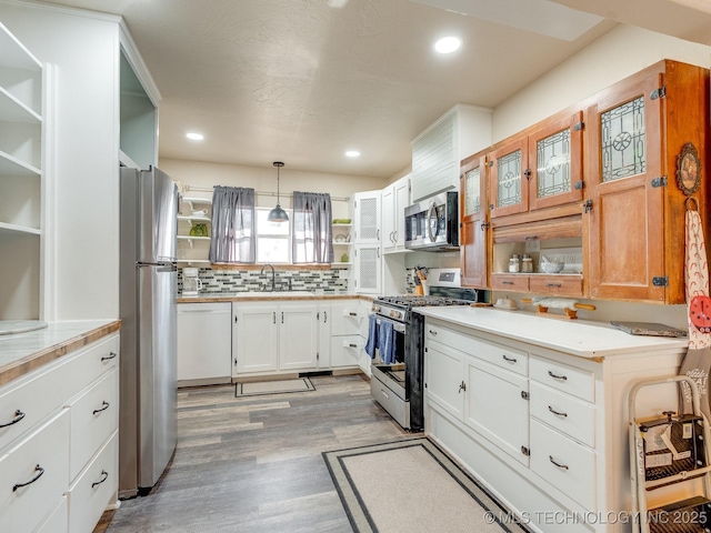 kitchen featuring backsplash, hanging light fixtures, appliances with stainless steel finishes, light hardwood / wood-style floors, and white cabinetry