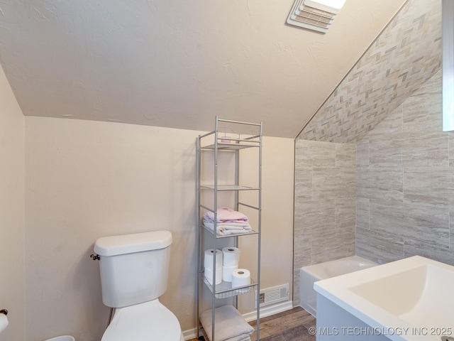 bathroom with a bath, hardwood / wood-style flooring, toilet, and lofted ceiling