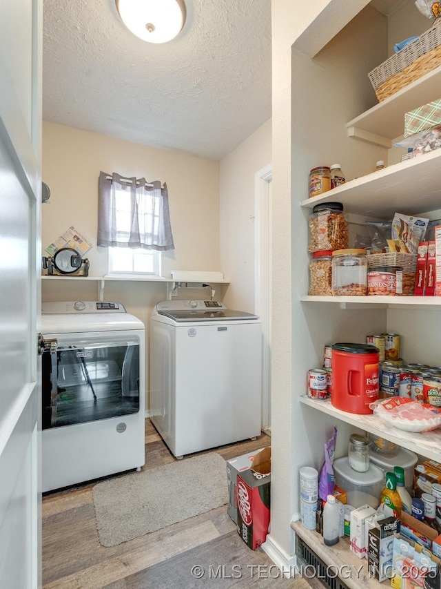 laundry room featuring a textured ceiling, light wood-type flooring, and washer and clothes dryer