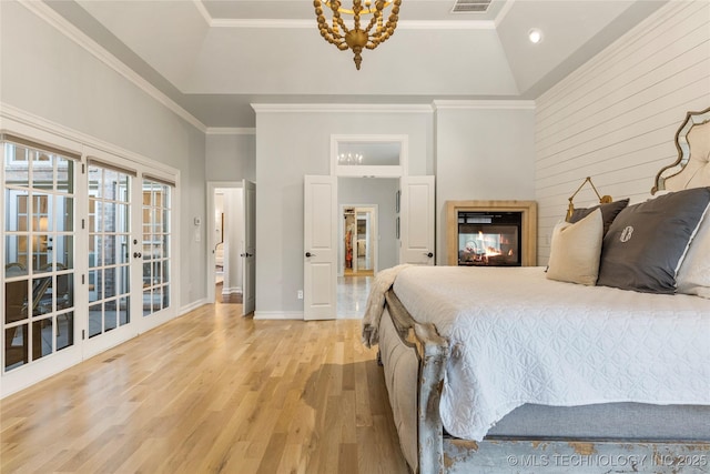 bedroom featuring french doors, crown molding, light hardwood / wood-style floors, lofted ceiling, and a tray ceiling