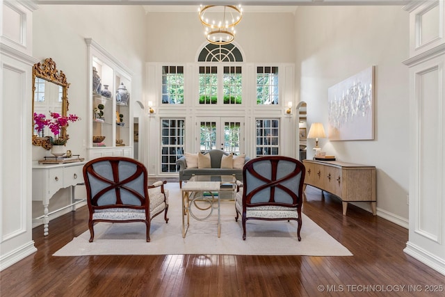 sitting room with french doors, dark wood-type flooring, a high ceiling, crown molding, and a chandelier