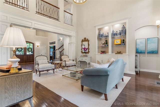 living room with built in shelves, dark hardwood / wood-style flooring, and a high ceiling