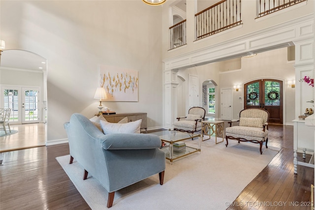 living room with dark hardwood / wood-style flooring, a towering ceiling, ornamental molding, and french doors