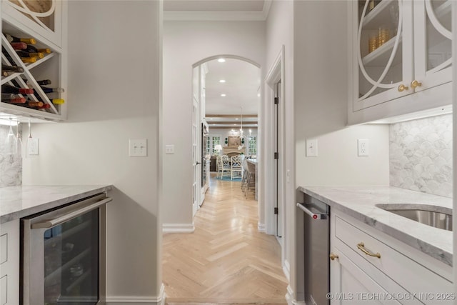 kitchen with wine cooler, light stone counters, light parquet flooring, crown molding, and white cabinets