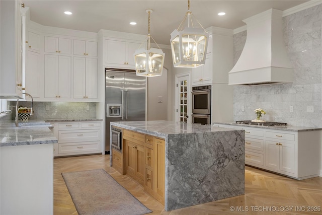 kitchen with white cabinets, custom exhaust hood, hanging light fixtures, and a large island