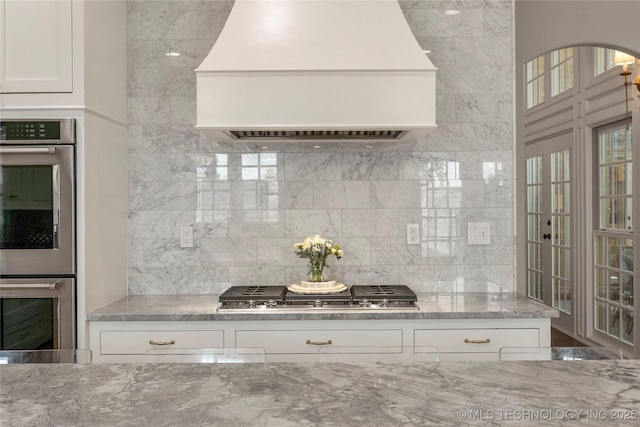 kitchen with tasteful backsplash, white cabinets, stainless steel appliances, and custom exhaust hood