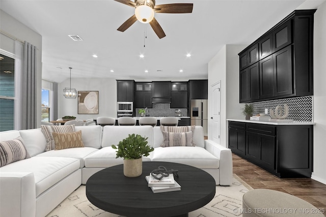 living room with sink, ceiling fan with notable chandelier, and light hardwood / wood-style flooring