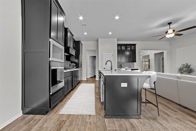 kitchen featuring a breakfast bar area, ceiling fan, appliances with stainless steel finishes, a kitchen island with sink, and backsplash