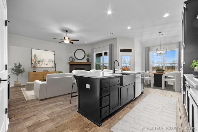 kitchen with ceiling fan with notable chandelier, an island with sink, dishwasher, sink, and hanging light fixtures