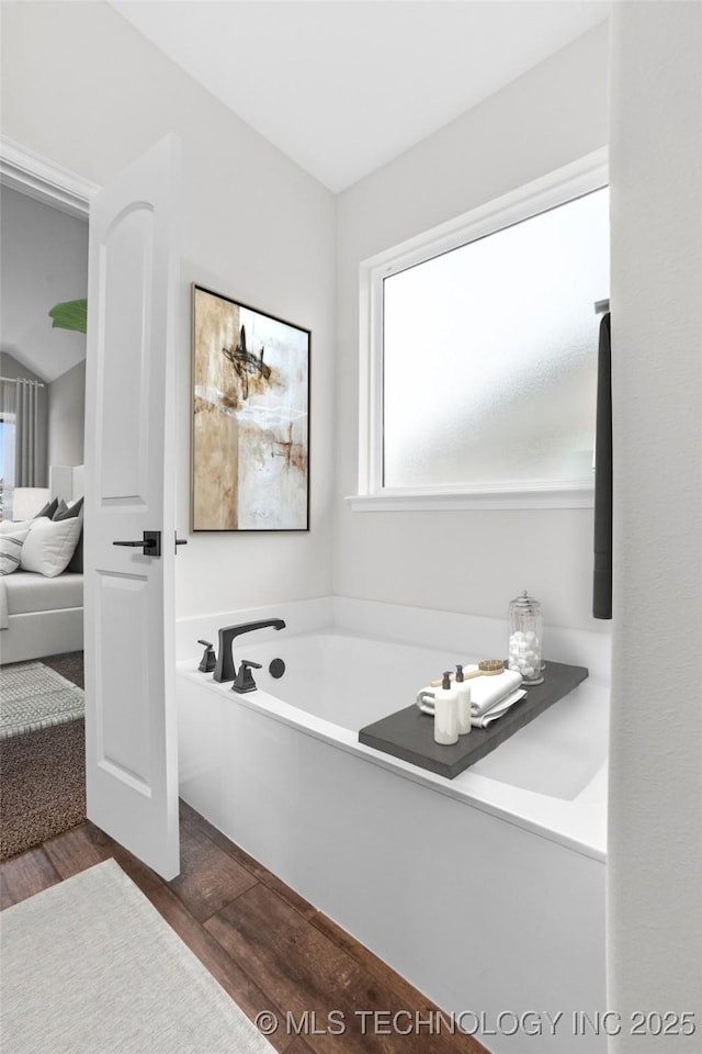 bathroom with vaulted ceiling, hardwood / wood-style floors, and a tub to relax in