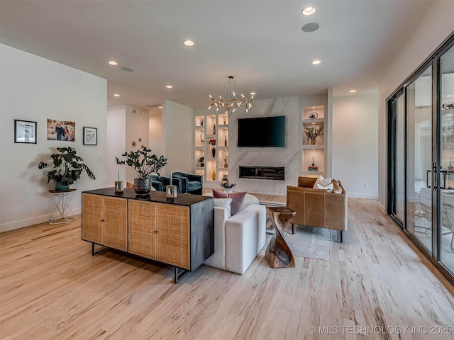 living room featuring a high end fireplace, built in shelves, light hardwood / wood-style flooring, and a notable chandelier