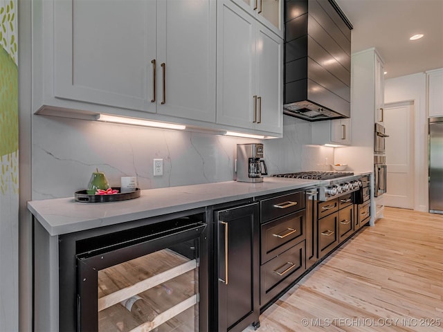 kitchen featuring premium range hood, wine cooler, light stone countertops, appliances with stainless steel finishes, and white cabinetry