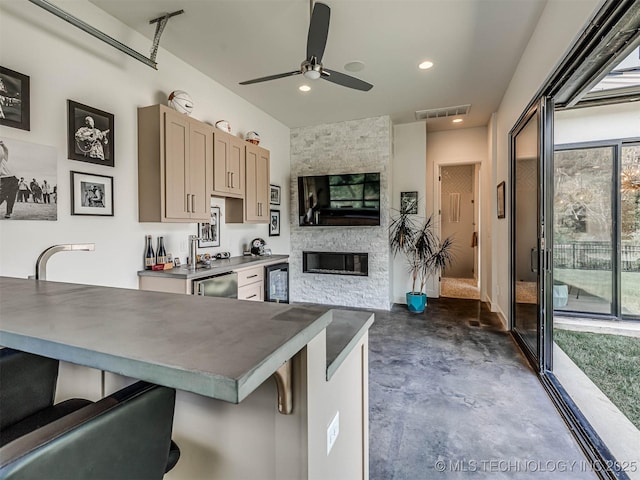 kitchen with light brown cabinets, wine cooler, ceiling fan, a fireplace, and a kitchen bar